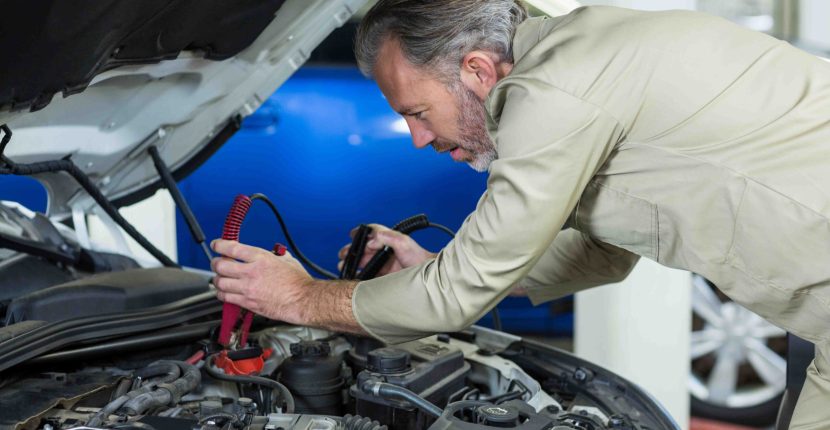 Mechanic attaching jumper cables to car battery in repair garage
